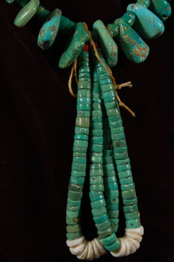 This is an exquisite Navajo turquoise nugget necklace comprised of beautiful dark green center- and off-center drilled turquoise stones and turquoise hieshe with a pair of jaclas. The turquoise hieshe is all hand-cut and hand-drilled. Most of the nugget turquoise stones are drilled off center, which is a favorite manner for pieces made for Native use. The turquoise is all-natural and untreated.  As we have stated many times, this style necklace is the most traditional of all necklaces that we associate with the Pueblo and Navajo cultures. Long before silver was introduced they were making necklaces of turquoise, hieshe, shell, coral and any other natural material. This is the style they were wearing when the Spaniards arrived in the 16th century; and this is the style they wear today during religious and social dances. This is a necklace often seen in historic photographs of both tribes.  In some necklaces, the hieshe beads strung between the nuggets are made from shell, but in this one, they are all drilled turquoise hieshe.  The only shells associated with this necklace are the white tips of the jaclas.  Condition:  The necklace is in excellent condition.  It has been re-strung and is ready for wear.  Provenance: from a gentleman in Florida 