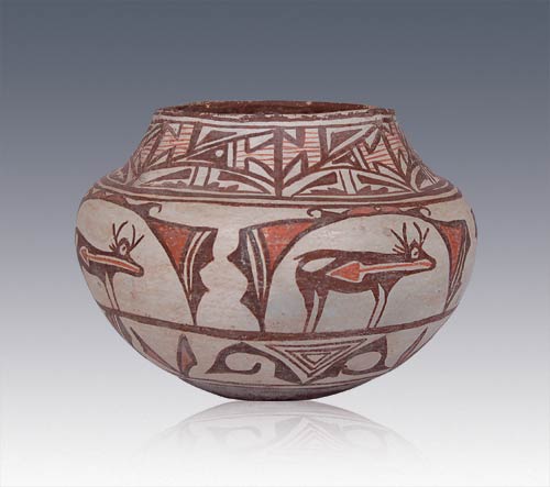 This is an exceptional early twentieth century Zuni Pueblo olla that has possibly seen some use at the pueblo. As is typical of Zuni polychrome wares after 1850, the vessel shape is somewhat squat, resulting in a slight enlargement of the mid-body. On the neck the decoration is quite elaborate. Note the stylized bird with its arrowhead body squeezed into a brown triangle. Adjacent to the bird element, within the rectangular block are brown outlines containing red parallel lines. The red parallel lines represent rain. Pueblo beliefs are that water jars are linked to rain. Invariably a potter will put some rain elements in the decoration. The main body of the vessel has a single row of heartline deer above a row of brown outline triangles and brown volute elements, below which is the brown bottom with a concave indentation. The vessel exhibits some wear around its rim, which consists only of some of the brown paint being worn off. There has been some repair at one point of the rim. Provenance: ex. Cody, Wyoming collection. This Zuni Polychrome Heartline Deer Jar was part of the exhibit CODY, WYOMING POTTERY COLLECTION June 10, 2006 until September 10, 2006 presented at Adobe Gallery Santa Fe.