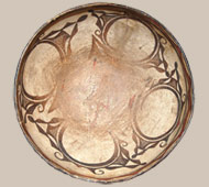 The majority of Zuni dough bowls seem to be 14 inches or less in diameter. Rarely do we see ones larger. That seems to be the standard for most of the ones from Zuni Pueblo. This one, however, is 16 inches in diameter. It dates to the last quarter of the nineteenth century. The paste materials are typically Zuni; white and chunky in texture with the centuries old temper material of ground pottery shards. The use of old shards for temper evidences the regard of the pueblo peoples for the old works made by their predecessors. To add these remnants to the new work is a sign of respect. The rim of the bowl is slightly indented from the exterior and has a distinctive inward curve on the interior, imparting a graceful shape to the bowl. The flexure of the interior of the rim flexes is a feature that seems to be standard on Zuni bowls. The bowl is slipped in traditional fashion with cream-colored clay, over which is painted the design in mineral and vegetal paints. The underbody is slipped in black, a tradition starting in the mid-1860s and continued to today. The exterior is decorated with traditional Zuni volutes that are an early portrayal of the Rainbird. The interior decoration begins with a brown rim below which is a wave-like element encircling the bowl that is painted red and outlined in brown. Below this are two wide parallel framing lines with a ceremonial break. Traditional Zuni volute design Rainbird elements fill the interior of the bowl down to the bottom, which then has a red element that appears as a four-pointed star. During a burglary of the Anthony residence in the 1990s, this bowl was taken along with everything else. When the entire collection was recovered a week later, a section of this bowl had been broken out. Fortunately it was recovered as well. The broken piece was professionally replaced. Collection Provenance: Edna Norton, who used to work in the pottery room of The Covered Wagon in Albuquerque