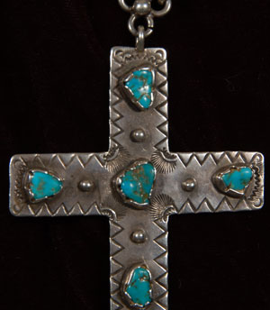 This cross was constructed from heavy gauge sterling silver.  It is stamped around all edges in a continuous line of triangles.  The four ends have smaller stamped triangles.  Six turquoise cabs are set on the cross is free-form silver bezels.  The handmade silver chain is attached to the cross with a three-circle hook.  The cross is stamped JP.  We have not identified the name of the artist.  Condition:  the cross and chain are in original condition.  It is estimated that the necklace dates to the 1970s.  Provenance:  from a gentleman in Florida 