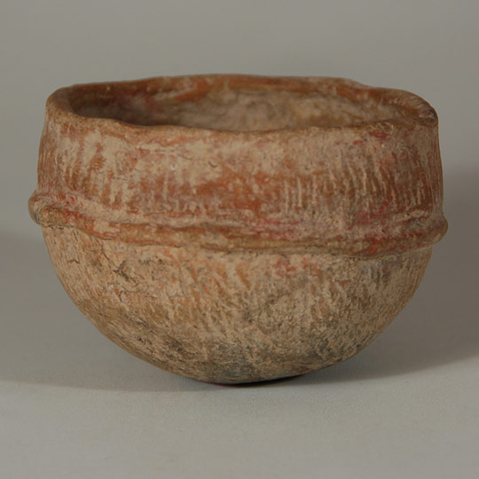 This small bowl almost has the feel of a stone metate or vessel for processing medication.  It is heavy in weight, appears to have been incised with lines over the entire exterior surface and painted with red pigment.  A single row of clay wraps around the vessel on the exterior.  It is so tempting to assign a function to it as possibly having been a paint jar or a medicine vessel, but there certainly is no way to do so.  It is what it was, whatever that might have been.   Condition: very good condition, with some unidentified residue on the interior. Provenance: from the collection of Katherine H. Rust Recommended Reading: Secrets of Casas Grandes, edited by Melissa S. Powell