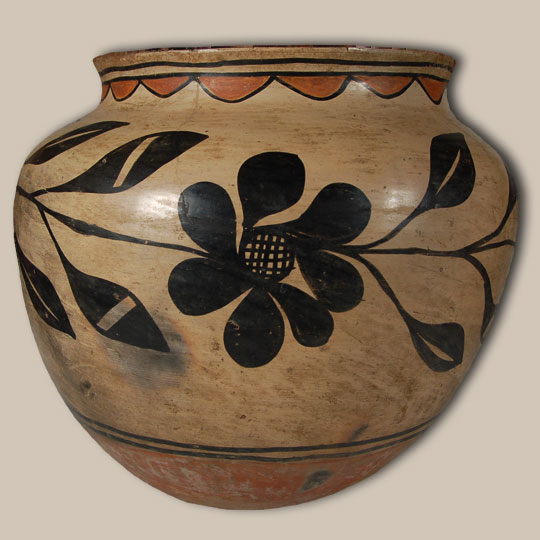 This storage jar was formed of native clay with typical crystalline rock temper. The underbody was not slipped but the natural tan clay of the vessel was stone-polished to a hard finish and the Kewa Pueblo distinctive large red band of rough polish, striated, soapy-like appearance was added below the design band.  This is indicative of a post-1880 date.   The bottom of the vessel is flat as is traditional with storage jars, unlike water jars that have a concave underbody.   The neck interior was slipped first in bentonite slip then red slip was rag-wiped over the bentonite leaving a quarter-inch of bentonite visible.  The rim top is black (a post-1800 characteristic). There is significant evidence of use. The rag-wiped bentonite slip is a wonderfully warm cream/off-white color, with subtle fire clouding and superb patina.   The entire body was designated for the design panel without a division separating the neck area from the body.  The large floral vegetal black design is typically Kewa Pueblo in origin with certain boldness and seemingly deliberate execution—a sure mark and fantastic sense of space and design. A series of semicircular elements, suggestive of clouds, are suspended from one of the two framing lines around the neck.  A second pair of framing lines encircles the vessel body at the base of the design.  All four framing lines feature ceremonial breaks.   This is a fantastic example of a Kewa Pueblo Polychrome jar with excellent patina, a warm/subtle glow to the white slip, and beautifully executed vegetal-black design elements.   Condition: There were several insignificant line cracks which have been repaired and an area of exfoliation due to water overflow that has been left in the natural state with no attempt to over-paint. This is a true find for the collector of the finest quality historic pueblo pottery from circa 1890-1910. Provenance: from the collection of a Phoenix ranching family. Recommended Reading: A River Apart: The Pottery of Cochiti and Santo Domingo Pueblos by Valerie K Verzuh