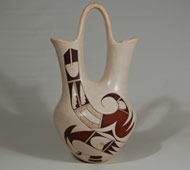 Joy Navasie is among the most famous of Hopi-Tewa potters. She learned the skill from her famous mother, Paqua Naha, the first Frog Woman. Paqua developed white-ware pottery in the mid-1950s and Joy continued the tradition until she ceased potting around 2000 due to health reasons.  She passed away in 2012.   This very large wedding vessel is typical of her graceful style. It has long curving necks connected by a tall arched handle. Joy's use of one large uncluttered design on each side adds to the cleanliness and elegance of the vessel.  The parrot design features the beak on the body of the vessel and a wing curving upward on one spout.  The other spout is without decoration.   Condition: excellent condition Provenance: from the collection of Dr. Allan Cooke, co-author of the book Canvas of Clay: Seven Centuries of Hopi Ceramic Art.  The jar was purchased by Dr. Cooke from a family from Detroit who had purchased it in 1960. Recommended Reading:  Canvas of Clay: Seven Centuries of Hopi Ceramic Art by Edwin L. Wade and Allan Cooke