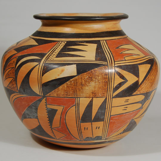 This wonderful Hopi polychrome small storage jar was probably made in the first half of the 20th century and could have been made by a member of the Nampeyo family, although not by Nampeyo.  At that time, Nampeyo had failing eyesight and would not have been able to apply the decoration, even if she had made the jar.  One of her daughters or some other Nampeyo family member certainly could have made it but we cannot be more definitive than that.    There are three storage jars of similar vessel shape in the book "The Legacy of a Master Potter: Nampeyo and Her Descendants" and that is our source for attributing the maker as a member of the Nampeyo family although the individual must remain unidentified.   The jar is magnificent, both in size, construction, and design.  The jar has been divided into four design panels, each outlined by three vertical black lines.  Within each panel, there are additional divisions into quarters.  Each quarter features a variety of designs, mostly geometrics.  There is a wide framing line near the base of the jar and another one at the neck, neither of which has a ceremonial line break.   Stippling, used by many members of the Nampeyo family, appears in each design panel.    The base of the jar is somewhat rounded, as is typical of jars that were made for actual use as they would be snuggled into a dirt floor.  Jars made for sale to collectors or tourists normally have a flat base.  The rim of the jar has an exaggerated flair outward similar to jars at Zuni Pueblo made for use as drums.  Overall, the jar has a beautiful warm glow to the yellow/orange slip.   Condition: the jar is in excellent condition Provenance: from the collection of Dr. Allan Cooke, co-author of the book Canvas of Clay: Seven Centuries of Hopi Ceramic Art.  Recommended Reading:  Canvas of Clay: Seven Centuries of Hopi Ceramic Art by Edwin L. Wade and Allan R. Cooke