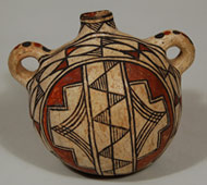 This is one of the most strikingly beautiful Laguna Pueblo canteens we have acquired in over a decade.  Not only does it have a bulbous front, it has a bulbous back as well.  The vessel sits on its base so that the design is easily visible.    The canteen was slipped in creamy white clay, polished to a smooth finish and that then became the canvas on which the artist began to execute her design. A circle outlined with a pair of thin black framing lines set the stage for the main body design which was then divided into a pair of semicircles split by a rectangular bar.  The bar was divided by a single black line down its middle from which black triangles are pendant and their directions are alternate.  The triangles were then filled with fine black lines.    The semicircles on the body were each designed with a stepped element inside which is a triangle formed with four black lines intersecting at an apex.  The area between the stepped elements was filled in with red. A wide band encircles the main body design and it contains a chain of triangles, some of which are filled in with red and alternating ones filled in with fine lines.   The back of the canteen is designed with a solid red center bordered by triangles of fine line elements that alternate directions.  The neck repeats such triangles, all of which are pendant from a framing line.  The rim is painted black, the interior of the rim painted red and alternating black and red dots adhere to the handles.  The canteen dates to the first quarter of the 20th century, probably circa 1920.   Condition: structurally in excellent condition with excellent condition of the painted design. Provenance: from an elderly lady in Santa Fe Recommended Reading: Acoma and Laguna Pottery by Rick Dillingham