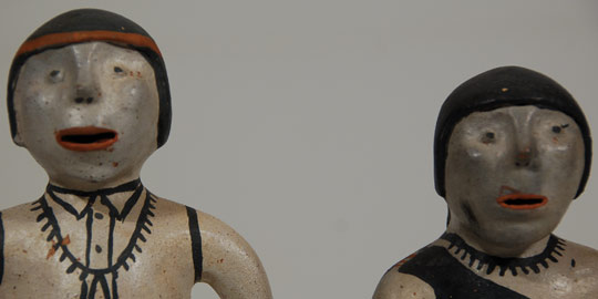 This male and female pottery figurine couple was obviously made as a pair and has been together since probably the mid-1970s when they were likely made.  Neither of the figurines is signed with the name of the maker but they were shown to Cochiti Pueblo potter Virgil Ortiz who said he believe they were made by Aurelia Suina.  Each of the figurines is dressed in traditional pueblo clothing.  The female is wearing the traditional pueblo dress that is over one shoulder and under the other.  It is cinched at the waist with a woven sash.  She is wearing traditional brown moccasins, a necklace and bracelets on both arms.  He is wearing a button-up shirt, also cinched at the waist with a woven belt.  He has on traditional moccasins, a red headband and jewelry on both wrists and a nugget necklace with jaclas.  Condition:  It is our speculation that these date to the 1970s and both figurines are in excellent structural condition with no evidence of repair of any kind.  There are a few scratches here and there but nothing of great significance. Provenance: from a client in Scottsdale, AZ Recommended Reading:  Clay People: Pueblo Indian Figurative Traditions by Jonathan Batkin 