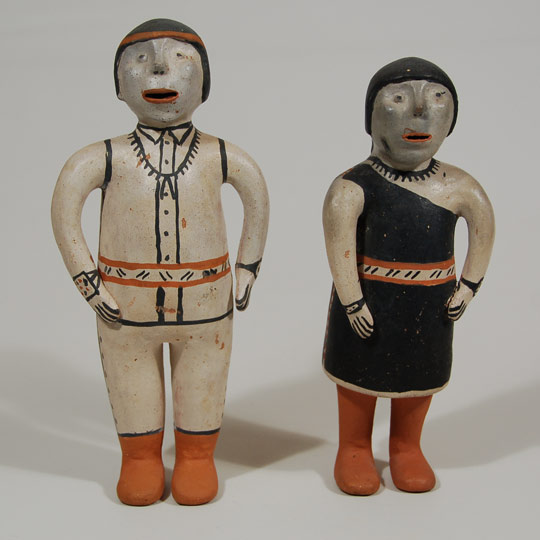 This male and female pottery figurine couple was obviously made as a pair and has been together since probably the mid-1970s when they were likely made.  Neither of the figurines is signed with the name of the maker but they were shown to Cochiti Pueblo potter Virgil Ortiz who said he believes they were made by Aurelia Suina.   Each of the figurines is dressed in traditional pueblo clothing.  The female is wearing the traditional pueblo dress that is over one shoulder and under the other.  It is cinched at the waist with a woven sash.  She is wearing traditional brown moccasins, a necklace and bracelets on both arms.  He is wearing a button-up shirt, also cinched at the waist with a woven belt.  He has on traditional moccasins, a red headband and jewelry on both wrists and a nugget necklace with jaclas.   Condition:  It is our speculation that these date to the 1970s and both figurines are in excellent structural condition with no evidence of repair of any kind.  There are a few scratches here and there but nothing of great significance. Provenance: from a client in Scottsdale, AZ Recommended Reading:  Clay People: Pueblo Indian Figurative Traditions by Jonathan Batkin