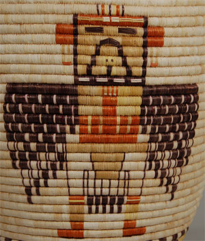 Baskets made by the women from Second Mesa villages are unique in the Southwest both for designs and construction techniques.  The coils are made from a bundle of galleta grass or rabbitbrush over which stitches of thin strips of yucca form the weft or outer layer.  The Hopi are unique in this technique as no other pueblo made baskets in this manner.  It is believed that it is a carryover from their prehistoric Hohokam ancestors.  The primary colors on Hopi coiled baskets are the natural shades of yucca leaves, from which the sewing splints are made.  The leaves in their natural state are green, when frozen are white and when bleached in the sun are golden yellow.  The yucca can be boiled with sunflower seeds, piñon pitch and ocher to obtain a black color.  Navajo tea provides for yellow-orange.    Large baskets with Katsina faces or full-body katsinas were made in the 1880 to 1900 period and have been revived in interest by today’s collectors.  This basket is larger than most being made today and it is spectacularly decorated with a pair of Crow Mother Katsinas and a pair of Eagle Katsinas.  According to Andrew Hunter Whiteford, “Contemporary coiled baskets from Second Mesa equal or surpass any made in earlier times.  Materials are carefully prepared, the baskets are tightly coiled and stitched, and large quantities of them are made as gifts, as ritual objects, and for sale to outsiders.”  This basket, made by Hopi artist, Elizabeth Nuvayumay, is spectacular in size, shape, construction and design.  The four images of full-body katsinas were brilliantly executed over the wonderful variegated background yellow yucca color.  It is an extraordinary work of art.  Condition: original condition Provenance: from an Arizona resident Recommended Reading; Southwest Indian Baskets: Their History and Their Makers by Andrew Hunter Whiteford 