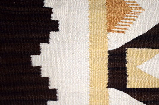 This rug from Crystal Trading Post displays an unusual use of the brown wool by the weaver’s choice of alternating shades of brown.  It is very subtle, but if examined closely, one can determine that the weaver used a half dozen or so rows of dark brown, then a half dozen or so rows of a lighter shade of brown, alternating throughout the textile.  This was carried out on the border and the brown wool in the interior design.  It gives life and interest to what could have been a lot of dark brown wool.  Her choice to alternate rows of shades of brown was ingenious and artistic.